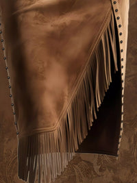 Brown leather chaps with fringes and studs on a textured brown background