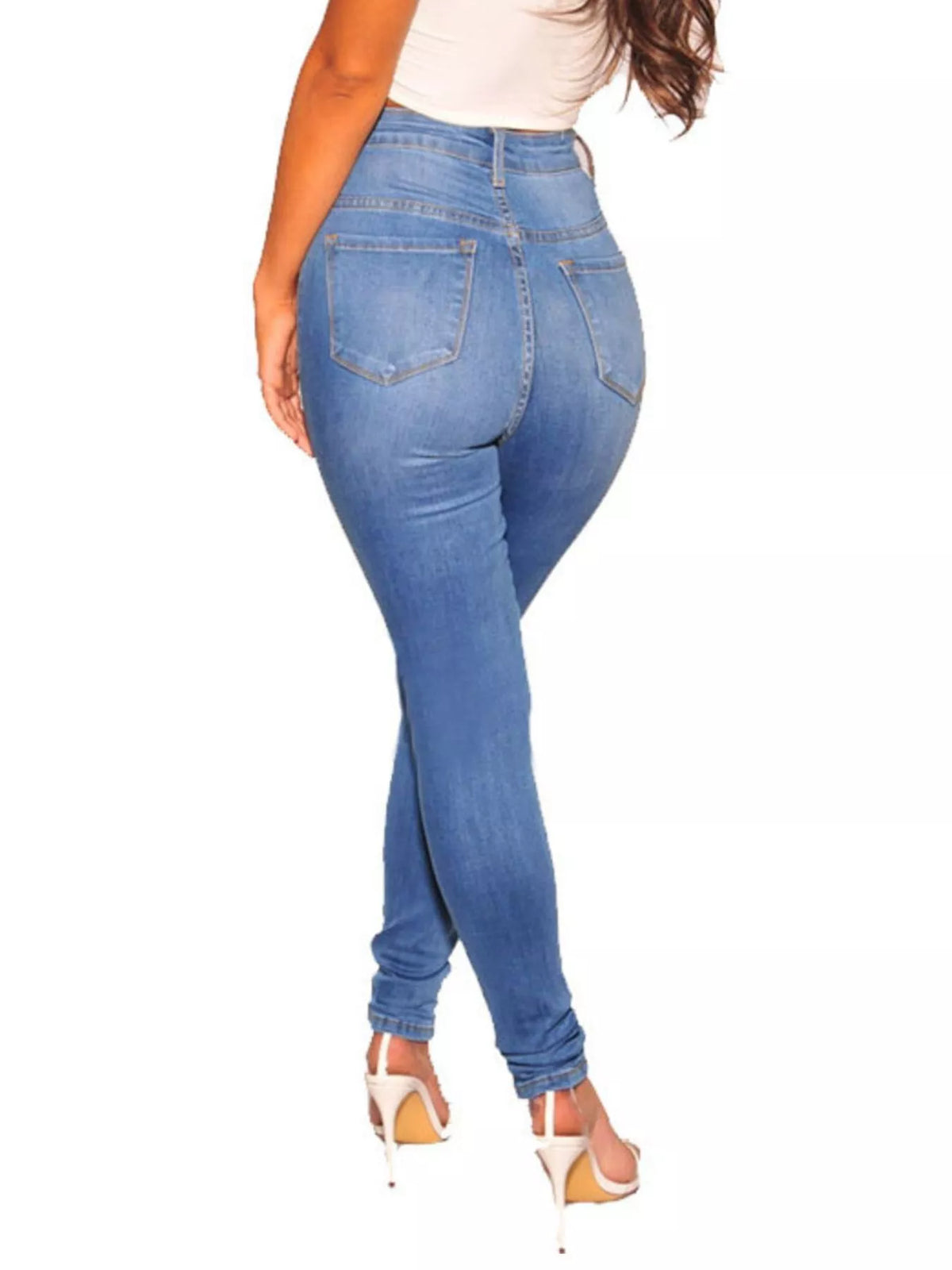 A model shown from the back wearing high-waisted, skinny blue jeans and white high-heeled sandals against a plain white background.
