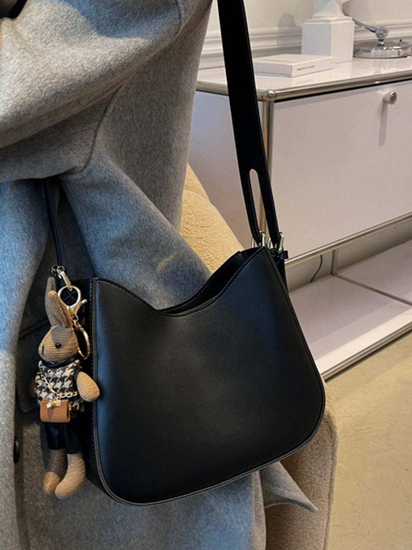 Black handbag with a rabbit keychain held by a person wearing a gray coat.