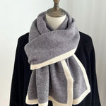 Gray scarf with white trim draped over a black garment on a mannequin against a white background