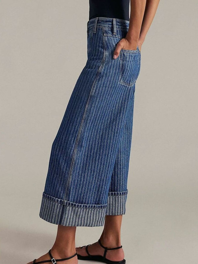 Long blue denim pants worn by a person on a neutral background