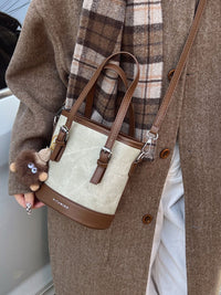 Person holding a beige and brown handbag with a plaid scarf and coat
