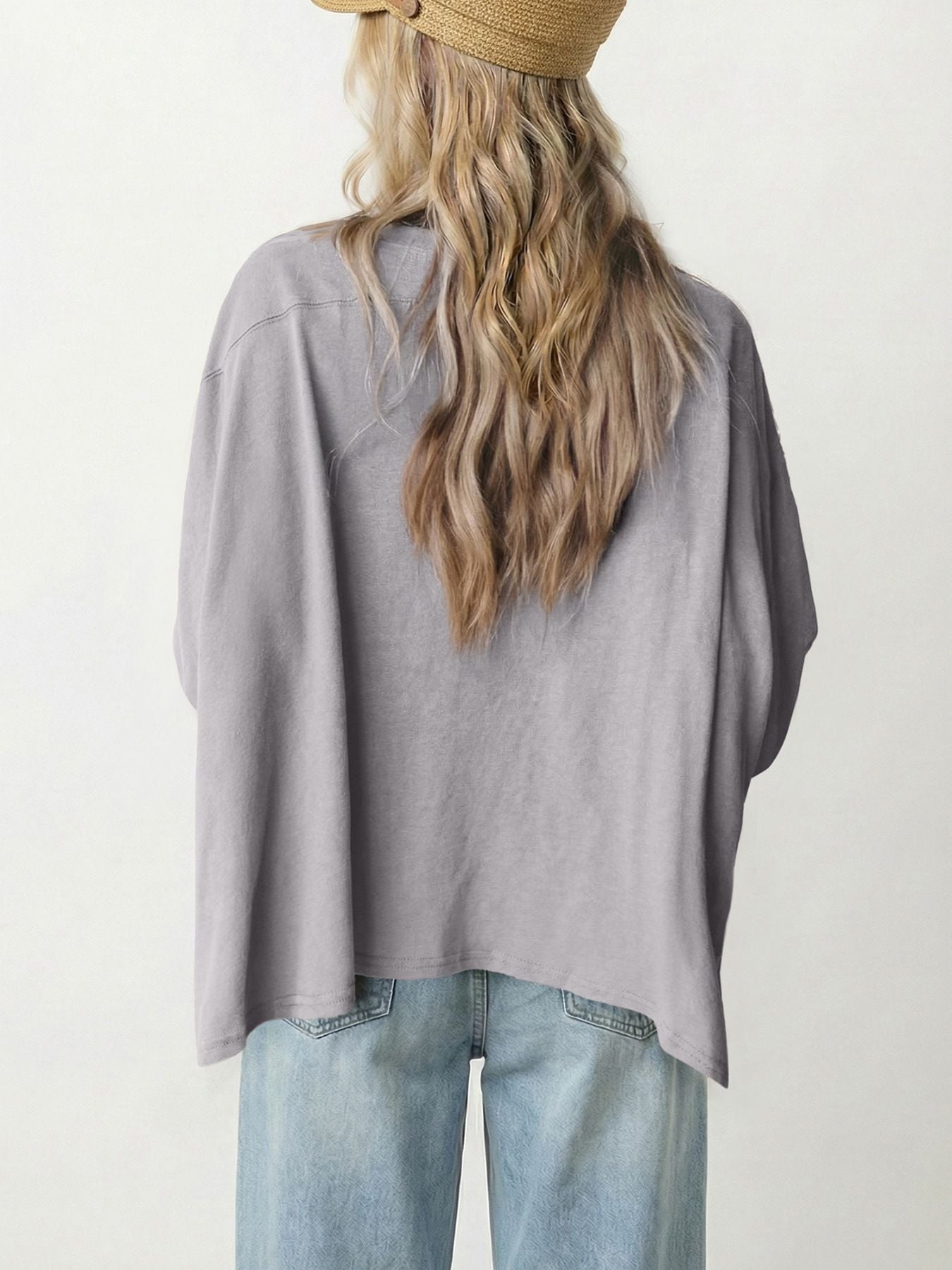 Person wearing a gray oversized shirt and light blue jeans with a neutral background