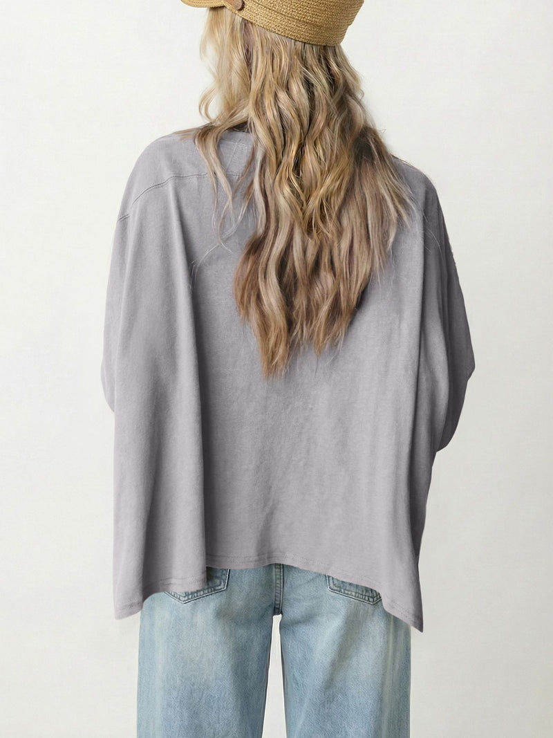 Person wearing a gray oversized shirt and light blue jeans with a neutral background