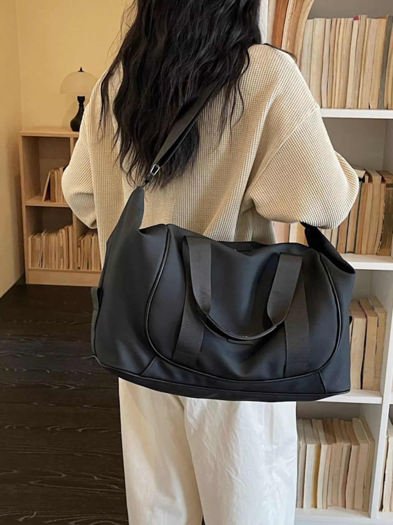 Person holding a black handbag in a room with bookshelves.