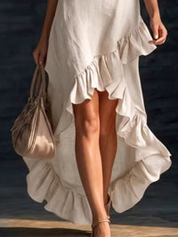 Woman in a white dress holding a beige handbag by the water