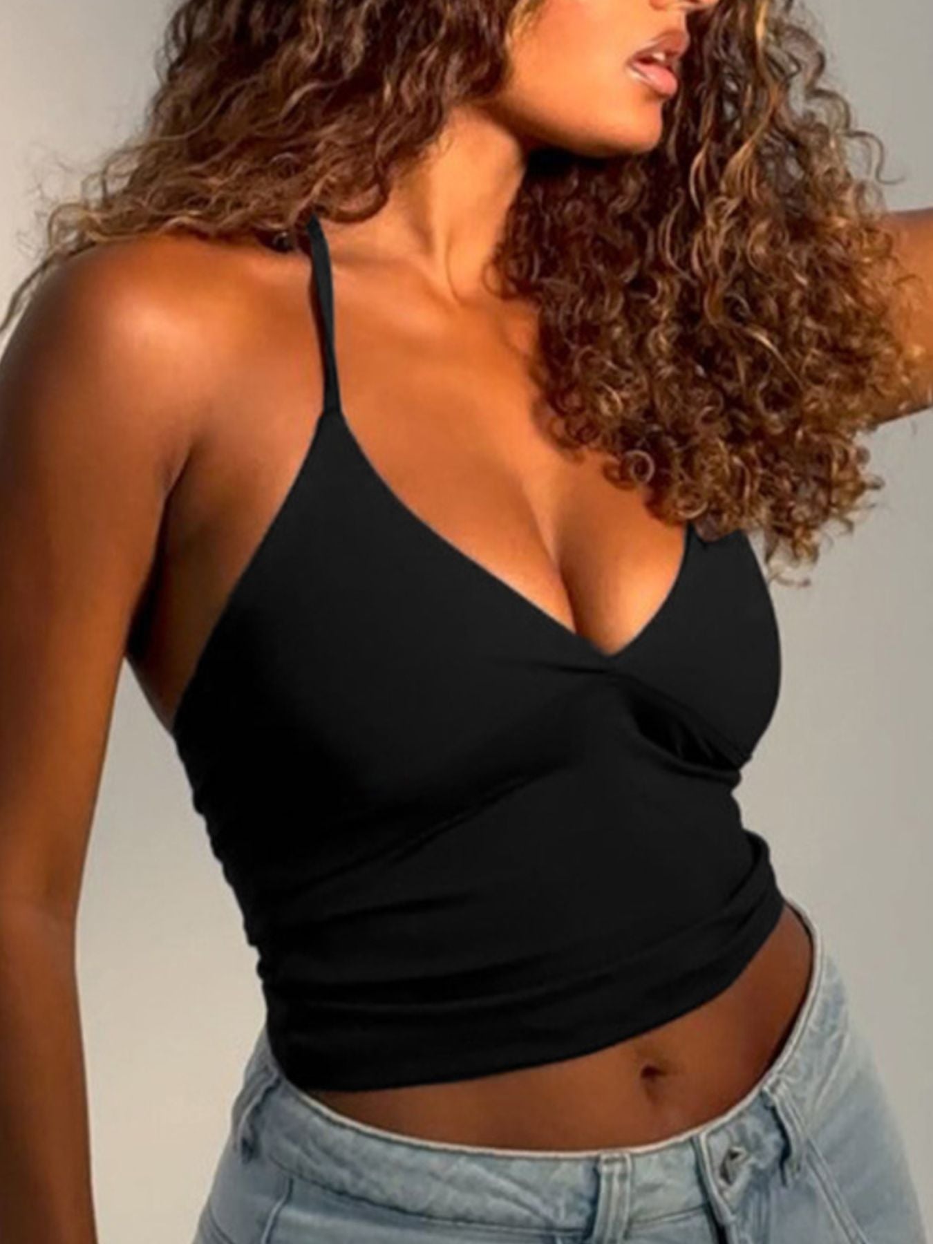 Woman wearing a black tank top and light blue jeans against a neutral background