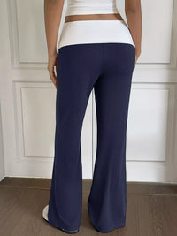 Person wearing navy blue flared pants and a white top against a neutral wall.