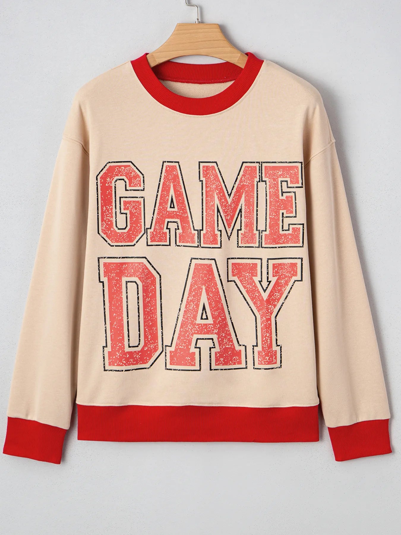 Beige sweatshirt with red 'GAME DAY' text on a hanger against a gray background