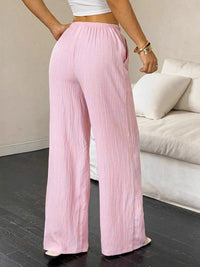 Person wearing light pink wide-leg pants in a room with a couch.