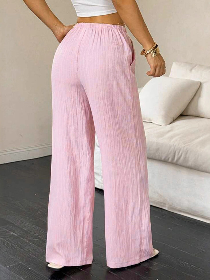 Person wearing light pink wide-leg pants in a room with a couch.