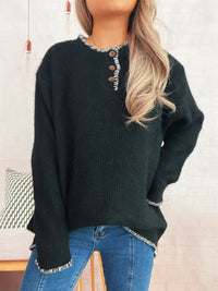 Person wearing a dark green sweater with button details and blue jeans against a neutral background