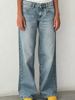 A person wearing light-wash blue wide-leg jeans, shown from the waist down against a plain light gray wall.