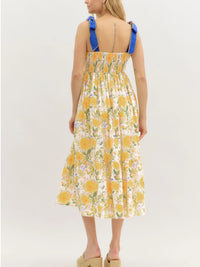 Woman wearing a yellow floral dress with blue straps on a white background