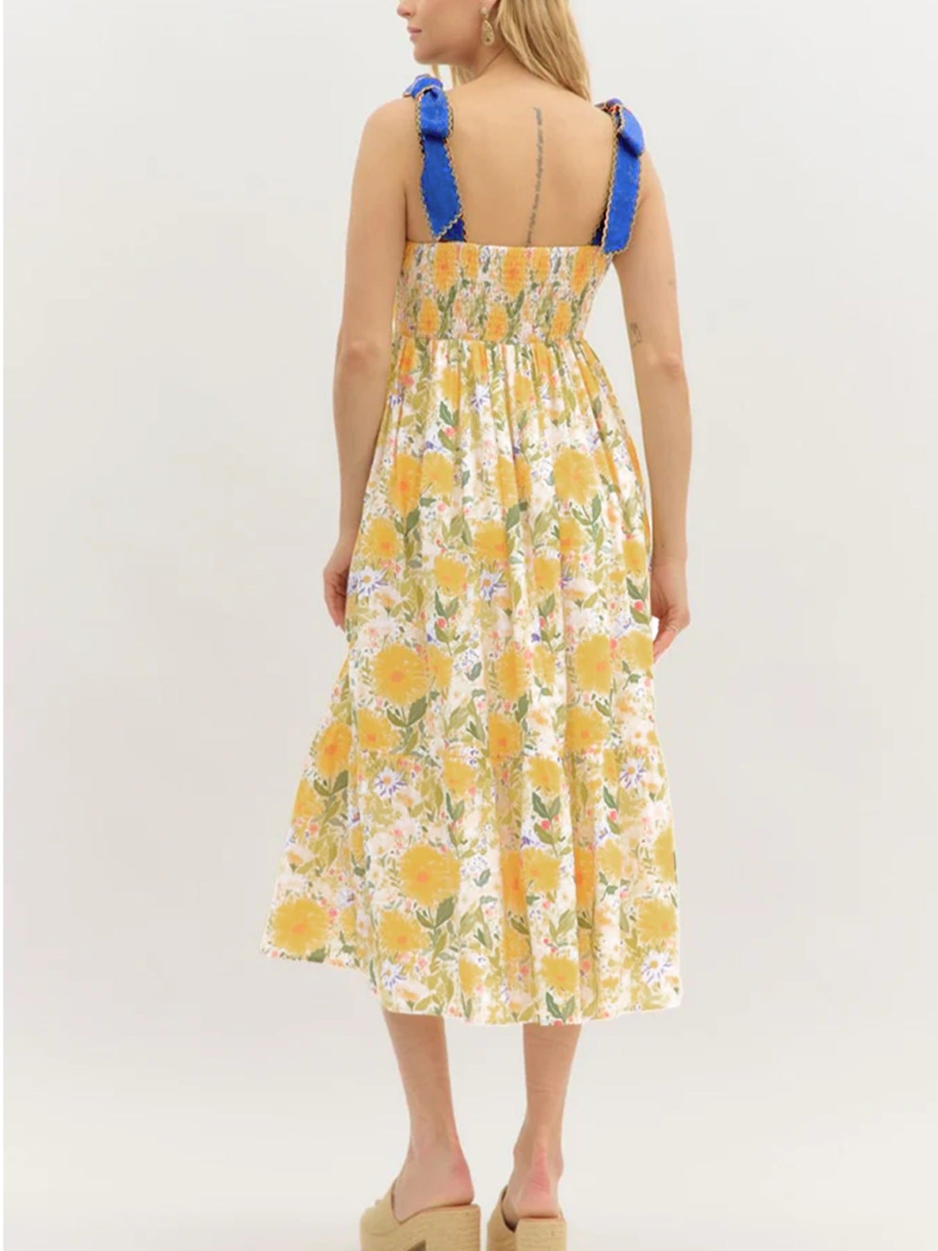 Woman wearing a yellow floral dress with blue straps on a white background
