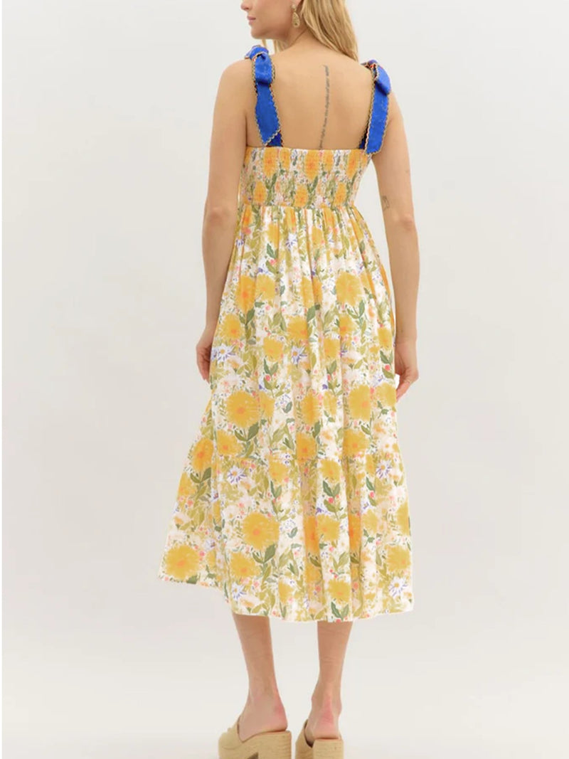 Woman wearing a yellow floral dress with blue straps on a white background