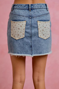 Denim skirt with floral pocket patches on a pink background