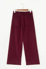A pair of wide-leg cropped trousers in deep burgundy corduroy, hanging on a wooden hanger against a plain white background.