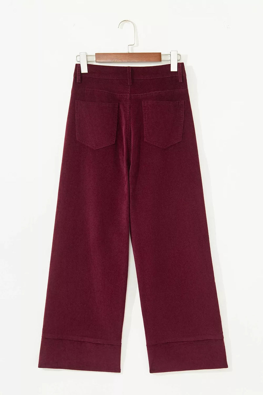 A pair of wide-leg cropped trousers in deep burgundy corduroy, hanging on a wooden hanger against a plain white background.