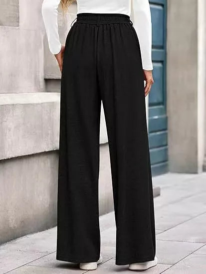 Person wearing black wide-leg pants and a white top in an urban setting.