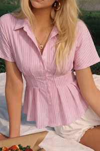 Woman wearing a pink striped shirt sitting outdoors with food on a table.
