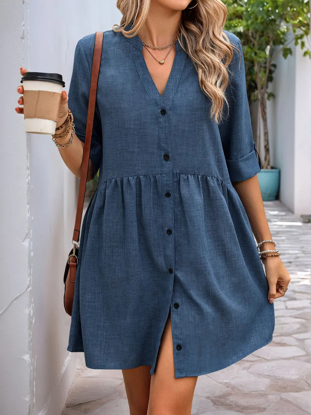 Woman wearing a blue dress holding a coffee cup outdoors.