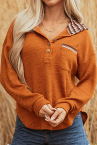 Person wearing an orange long-sleeve shirt with a patterned collar in a field.
