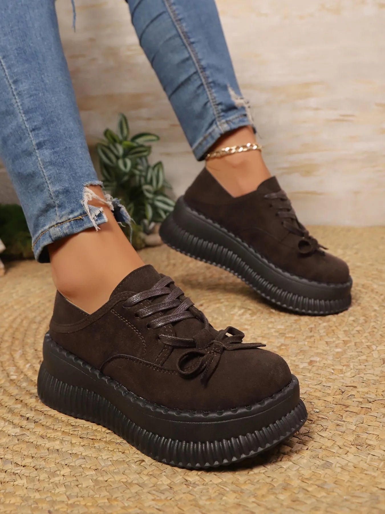 Brown platform shoes worn with blue jeans on a textured surface.