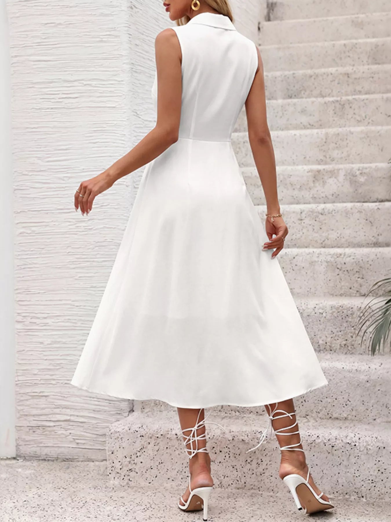 Woman wearing a white sleeveless dress standing on stone steps.