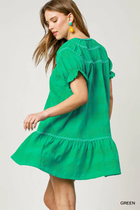 Woman wearing a green dress with ruffled sleeves and hem on a white background