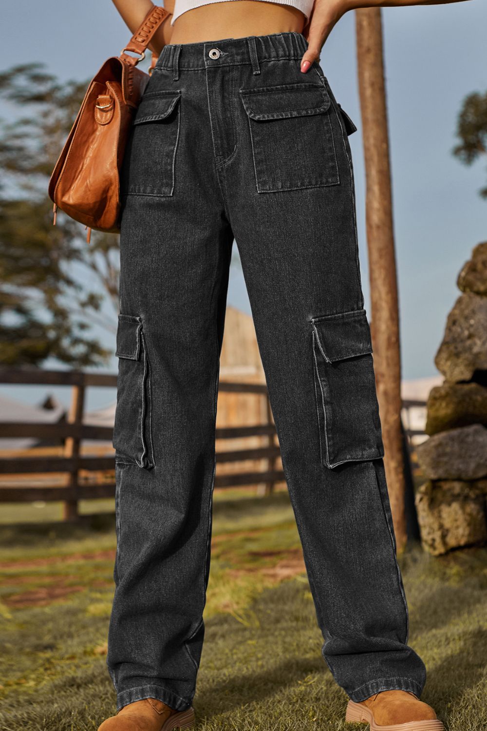 Person wearing dark gray cargo pants with a brown leather bag outdoors.