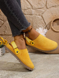 Yellow suede clogs worn with dark jeans against a stone wall background
