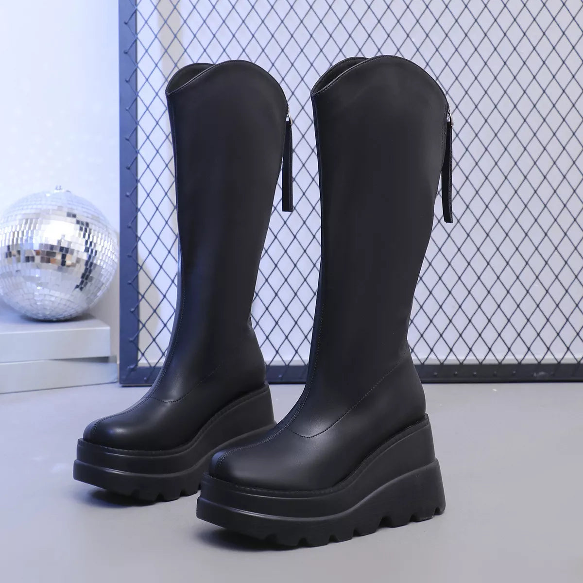 Black rubber boots with thick soles on a light gray surface.