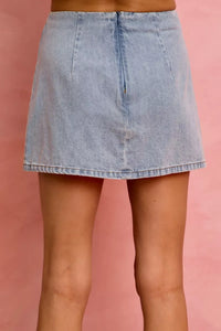 Light blue denim skirt worn by a person on a pink background