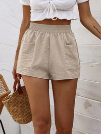 Person wearing beige shorts and a white top against a light wooden panel background