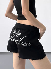 Black shorts with 'Lucky Butterflies' text worn by a person on a plain background