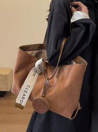 Brown leather tote bag with a strap featuring 'Kleavy' branding, held by a person wearing a dark coat.