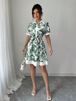 Woman wearing a green and white floral dress in a room with gray flooring and white curtains.