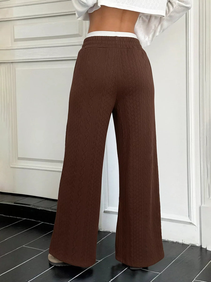 Brown wide-leg pants worn by a person in a room with white walls and black tiles.