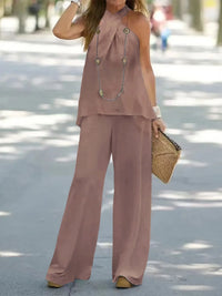 Woman wearing a pink outfit with wide-leg pants and a top, holding a straw bag on a street.
