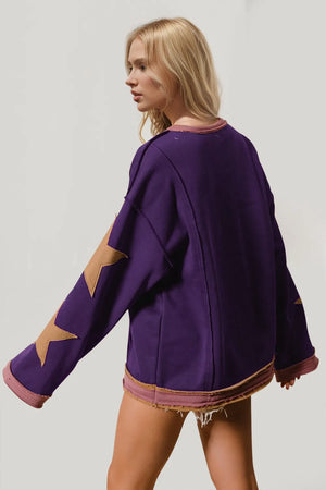 Woman wearing a purple sweater with star designs on sleeves against a plain background