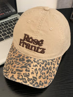 Beige cap with leopard print brim and 'Rose Frantz' embroidery on a black surface.