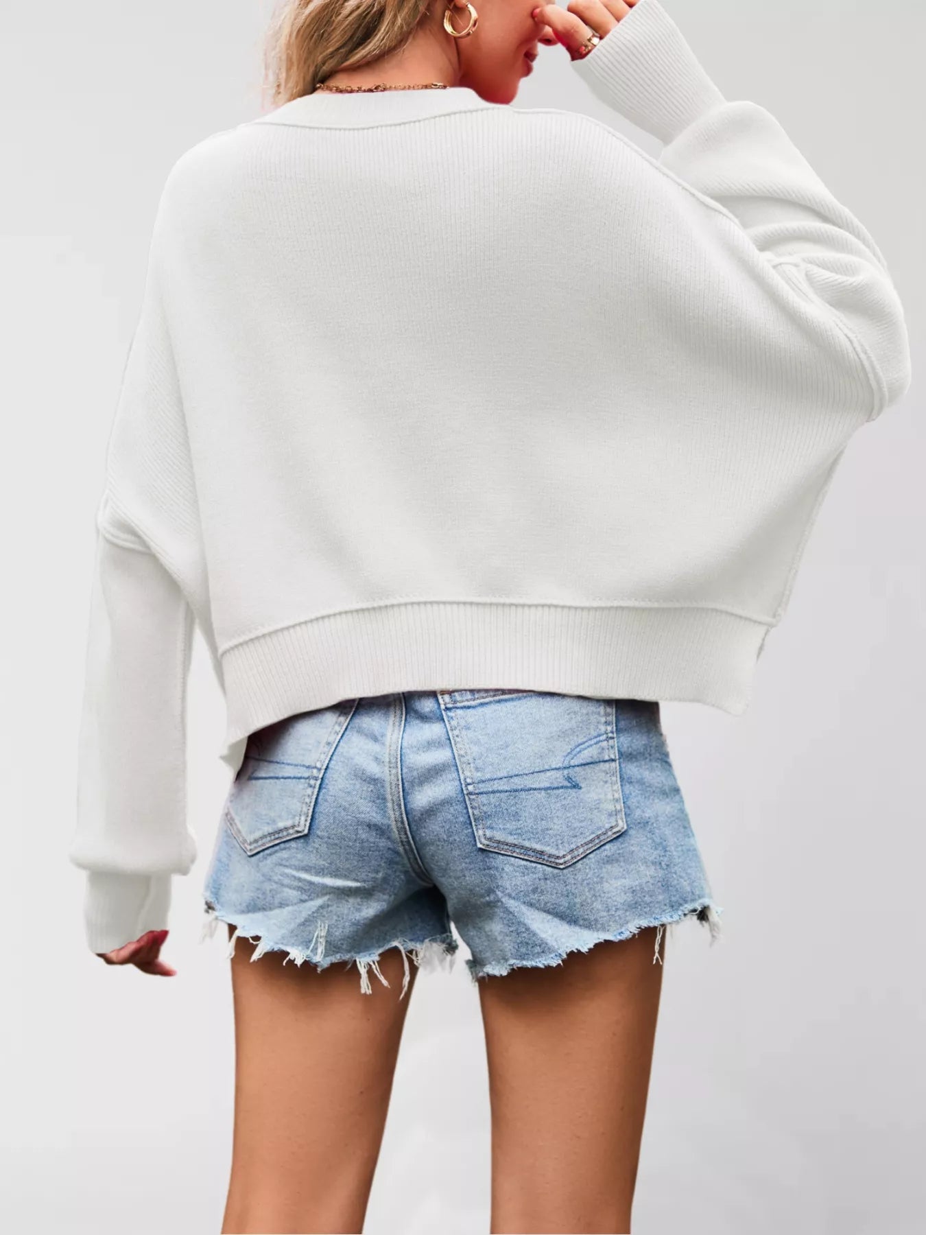 Person wearing a light gray sweatshirt and denim shorts on a plain background