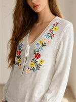 White sweater with colorful floral embroidery on a neutral background