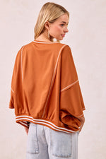 Woman wearing a rust-colored oversized sweater with white stripes on a plain background