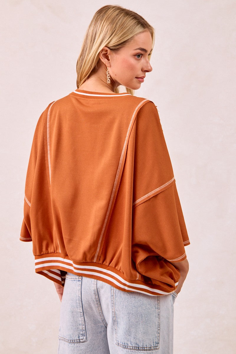 Woman wearing a rust-colored oversized sweater with white stripes on a plain background