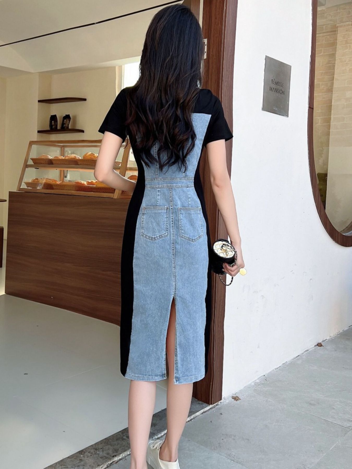 Woman wearing a black and denim dress standing in front of a store entrance.