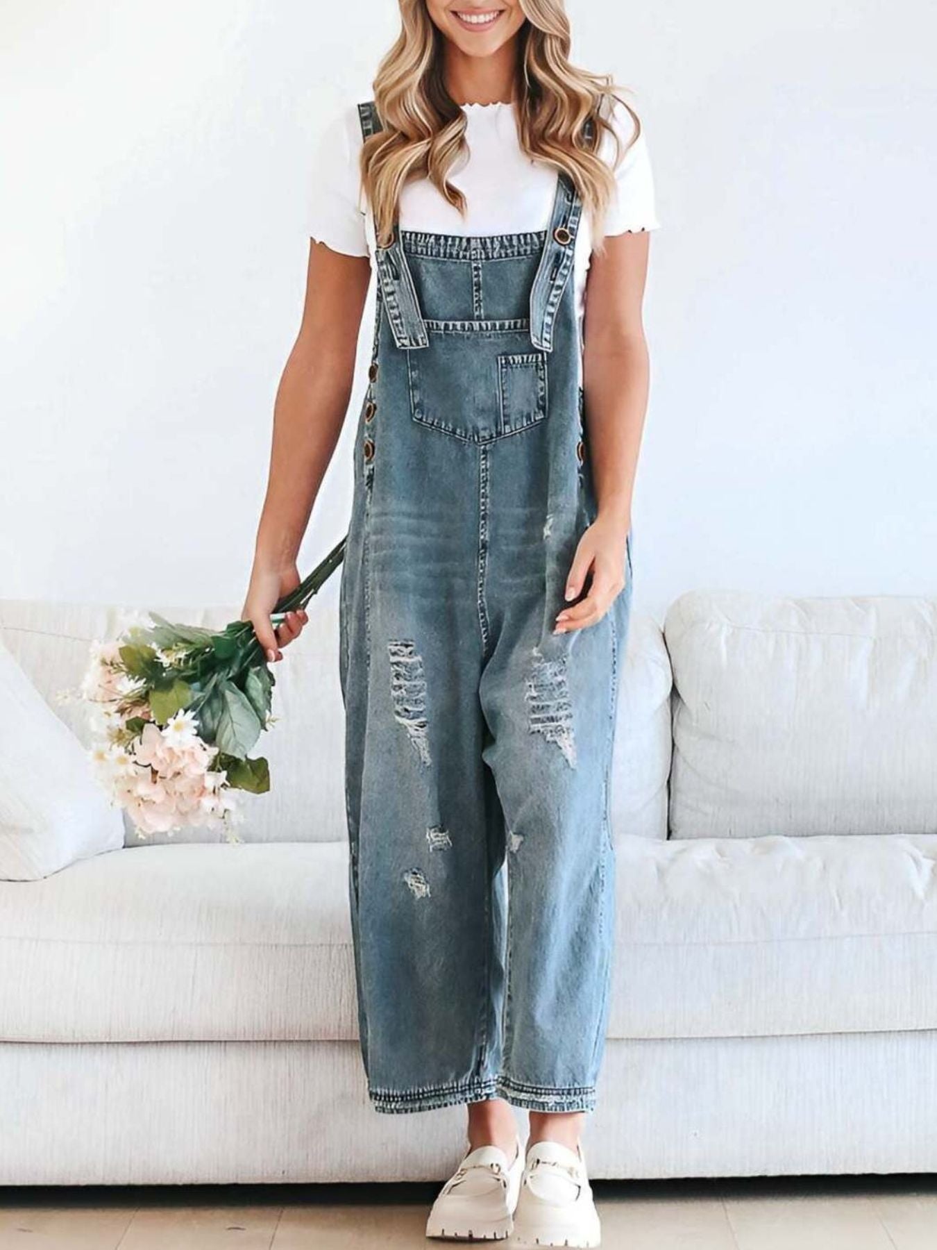 Person wearing denim overalls holding flowers in a living room setting