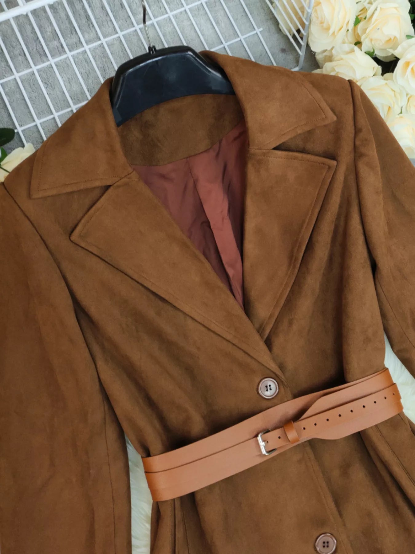 Brown coat with a belt on a hanger against a neutral background