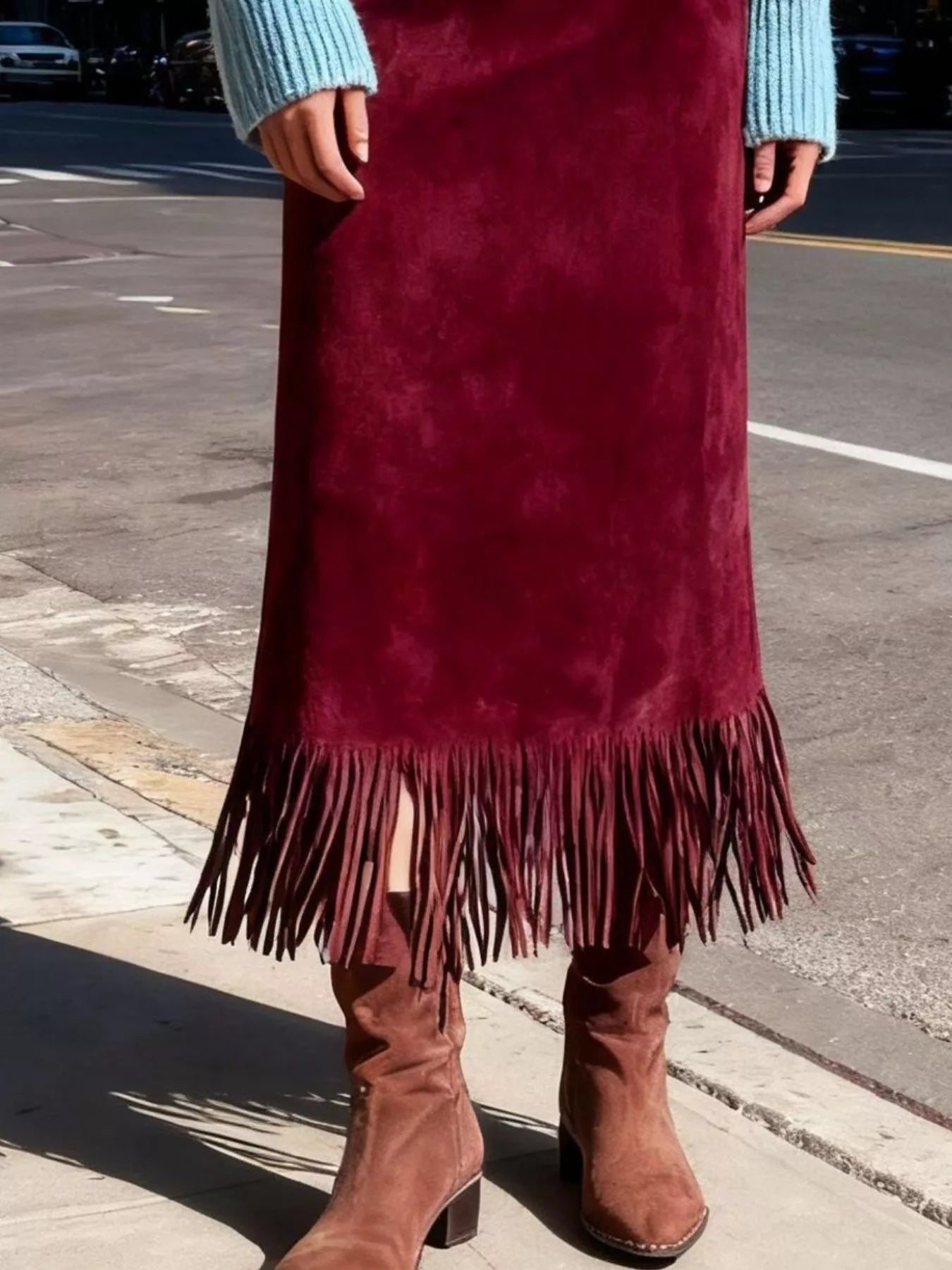 Person wearing a burgundy suede skirt with fringe and brown boots on a street.